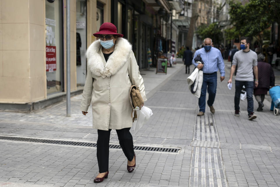 A woman wearing a hat and a protective face mask walk in central Athens, on Monday, April 5, 2021. Retail stores across most of Greece have been allowed to reopen despite an ongoing surge in COVID-19 infections, as the country battled to emerge from deep recession.(AP Photo/Petros Giannakouris)