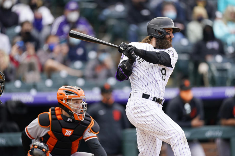 Colorado Rockies' Charlie Blackmon follows through on a two-run single next to San Francisco Giants catcher Buster Posey during the fourth inning of a baseball game Wednesday, May 5, 2021, in Denver. (AP Photo/David Zalubowski)