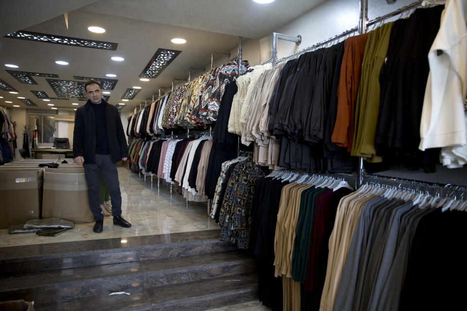 In this Wednesday, Feb. 12, 2020 photo, Palestinian shopkeeper Bilal Dwaik poses for a photo in his store, which sells clothes he imports from China, in the West Bank city Hebron. The local market has long been flooded by low-cost Chinese goods. Traders fear that if the outbreak and quarantine efforts continue they will have to switch to more expensive alternatives, passing higher prices onto consumers who may not be able to bear them. (AP Photo/Majdi Mohammed)