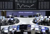 Traders are pictured at their desks in front of the DAX board at the Frankfurt stock exchange