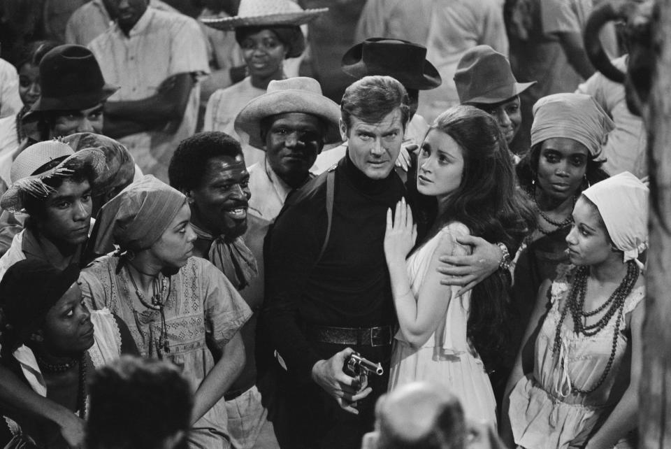 English actors Roger Moore and Jane Seymour surrounded by extras from the fictional Caribbean island of San Monique in the James Bond film 'Live And Let Die', being filmed at Pinewood Studios in England, 8th February 1973. (Photo by Milne/Express/Hulton Archive/Getty Images)