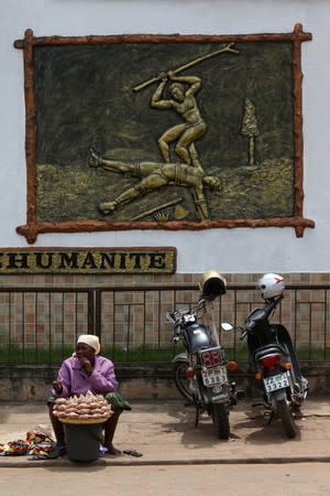Woman waits for customers as she sells her wares in front of a bas-relief of slaves embedded on the wall of Da-Silva museum at Porto-Novo, Benin