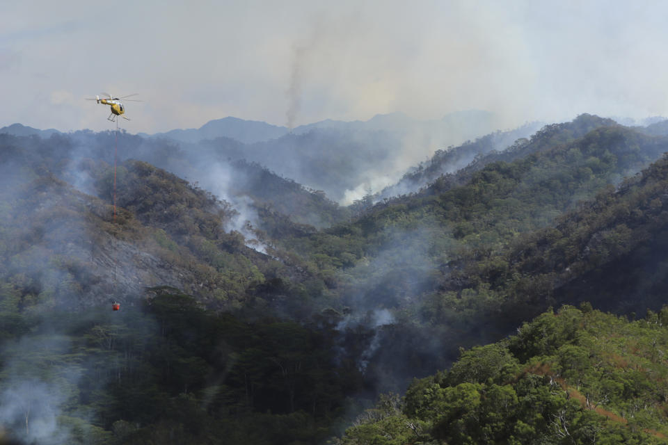 This photo provided by the Hawaii Department of Land and Natural Resources shows an Army helicopter carrying water to douse a wildfire burning east of Mililani, Hawaii, on Thursday, Nov. 2, 2023. A wildfire that has burned forestlands in a remote mountainous area of Central Oahu has moved eastward and away from population centers as firefighters continued to battle the blaze. (Dan Dennison/Hawaii Department of Land and Natural Resources via AP)