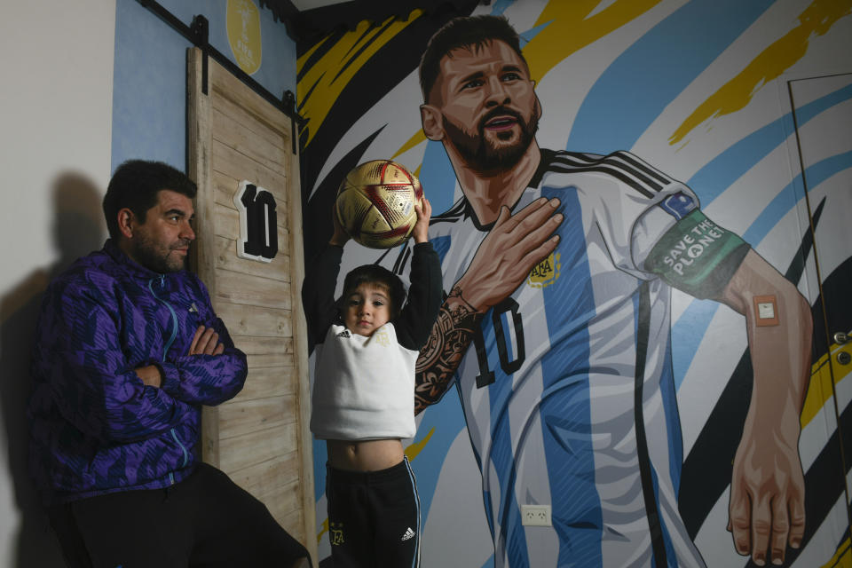 El aficionado argentino Matías Celestino y su hijo Benito Lionel posan para una foto en la habitación de Benito frente a una bandera con la imagen de Lionel Messi en su residencia en Buenos Aires, Argentina, el lunes 3 de junio de 2024. La familia de Celestino viajará a Estados Unidos para seguir la Copa América. (AP Foto/Gustavo Garello)