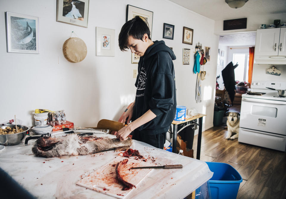 Iris&rsquo;s son Tanner cuts up caribou meat at his grandmother&rsquo;s home. (Photo: Angela Gzowski for HuffPost)