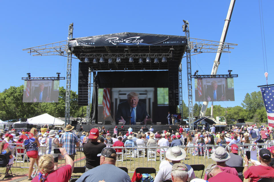 Former President Donald Trump addresses the crowd via video Saturday, June 12, 2021, at the River's Edge Apple River Concert Venue in New Richmond, Wis. The MAGA rally was organized by pillow salesman-turned conspiracy peddler Mike Lindell. For a few hours last weekend, thousands of Donald Trump’s loyal supporters came together under the blazing sun in a field in western Wisconsin to live in an alternate reality where the former president was still in office — or would soon return. (AP Photo/Jill Colvin)