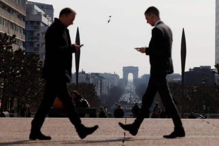 Men look at their mobile phones as they walk on the esplanade of La Defense in the financial and business district of La Defense, west of Paris, France March 26, 2018. REUTERS/Gonzalo Fuentes