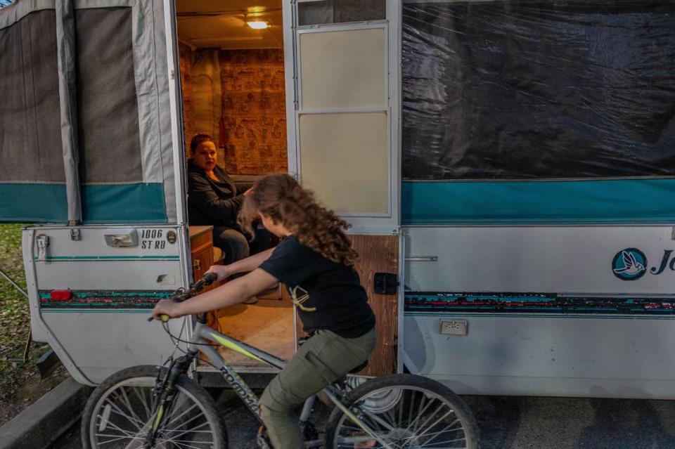 Kristi Phillips takes a break working on housing applications in her camper as her daughter Aryanna rides by in January 2021. The family of five was camping in South Natomas Community Park at the time.