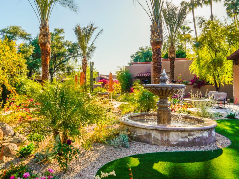 A fountain in front of an adobe building on the left in a garden with succulents, flowers, and palm trees at Hermosa Inn
