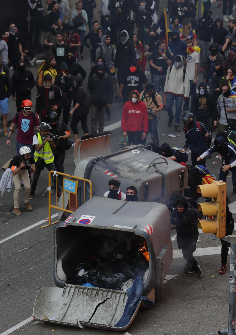 Protesters stand behind trash containers used as barricades on the fifth day of protests over the conviction of a dozen Catalan independence leaders in Barcelona, Spain, Friday, Oct. 18, 2019. Tens of thousands of flag-waving demonstrators demanding Catalonia's independence and the release from prison of their separatist leaders have flooded downtown Barcelona. The protesters have poured into the city after some of them walked for three days in "Freedom marches" from towns across the northeastern Spanish region, joining students and workers who have also taken to the streets on a general strike day. (AP Photo/Manu Fernandez)