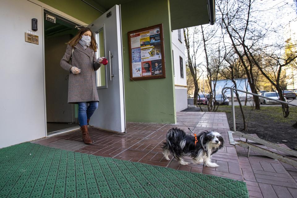 In this photo taken on Monday, April 27, 2020, volunteer Nadezhda Minyaeva, wearing a face mask and gloves to protect from coronavirus, with Russian pensioner Margarita Donchenko's dog Sopha leaves a porch of the apartment building for a walk in Moscow, Russia. Donchenko knows how much attention a dog needs and she is glad that when she can't give her fluffy little black-and-white pooch what she needs, there's volunteer Nadezhda Minyaeva to show up once a day for a walk. (AP Photo/Alexander Zemlianichenko)