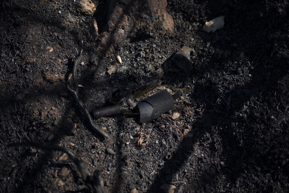 A broken wine bottle is pictured in the soil of a charred vineyard at Chateau des Bertrands in Cannet-des-Maures, southern France, Thursday, Aug. 26, 2021. Winemakers near the French Riviera are taking stock of the damage after a wildfire blazed through a once picturesque nature reserve near the French Riviera. The blaze left two people dead, more than 20 injured and forced some 10,000 people to be evacuated. (AP Photo/Daniel Cole)