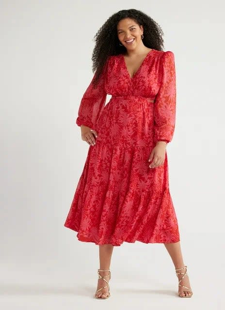 model in patterned red midi dress with long sleeves and V-neckline, standing with hands on hips