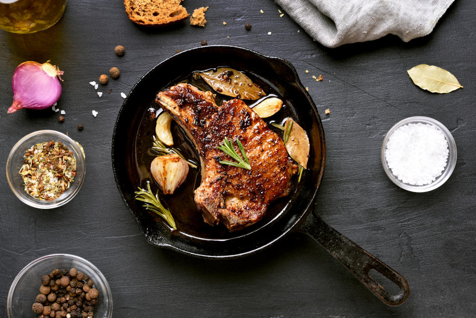 Grilled pork steak in frying pan over dark background, top view