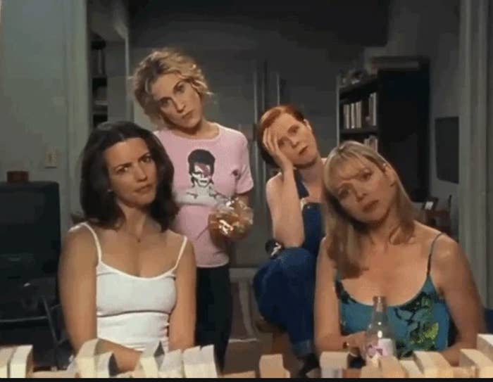 Sarah Jessica Parker, Kristin Davis, Cynthia Nixon, and Kim Cattrall are sitting together, each with distinct expressions, in a scene suggesting a casual chat