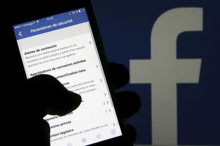 A man reads parameters of security on his phone in front of a displayed Facebook logo in Bordeaux, southwestern France, March 10, 2016. REUTERS/Regis Duvignau/Illustration