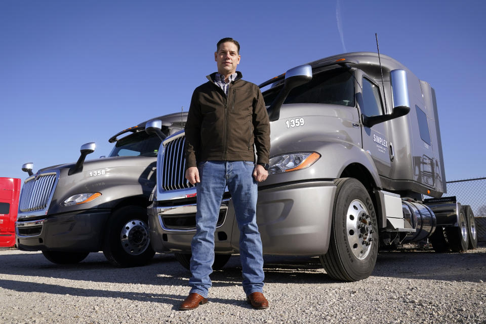 Aaron Tennant stands in front of vehicles in the lot of his trucking and shipping company, Monday, Dec. 20, 2021, in Colona, Ill. Tennant owns trucking and shipping companies on both the Iowa and Illinois sides of the Mississippi River. This month, after six years under construction, a new bridge opened connecting the town of Bettendorf, Iowa and Moline, Illinois on Interstate 74. But last summer's delays cost Tennant productivity. It frustrated commuters and added extra stress to older bridges. (AP Photo/Charlie Neibergall)