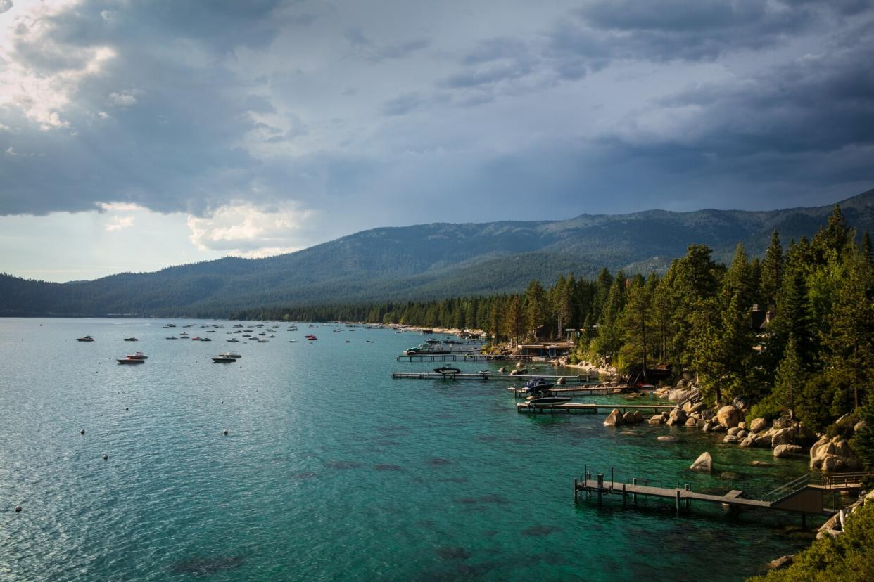 The Lake Tahoe shoreline with boats in the water and trees and big rocks along the shore.