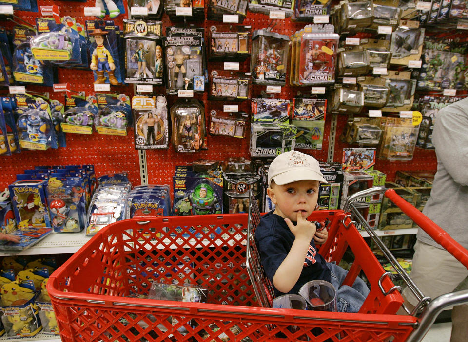 A young boy sits in his parents shopping cart in the midst of a toy aisle at a Target store.