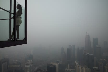 A tourist poses for a picture at Kuala Lumpur Tower with the city skyline in the background shrouded by haze, in Kuala Lumpur