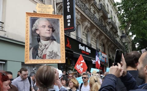 People hold placard depicting French President Emmanuel Macron as a monarch and reading 'Restoration of the monarchy' - Credit: JACQUES DEMARTHON/ AFP