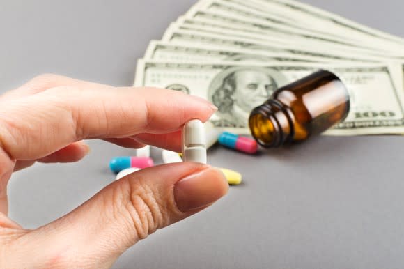 Hand holding pill with cash and other pills on table