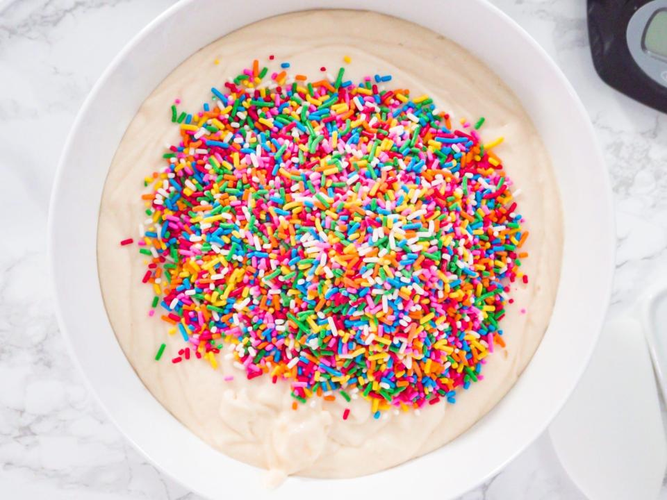 sprinkles added to vanilla cake batter in a bowl on a kitchen counter