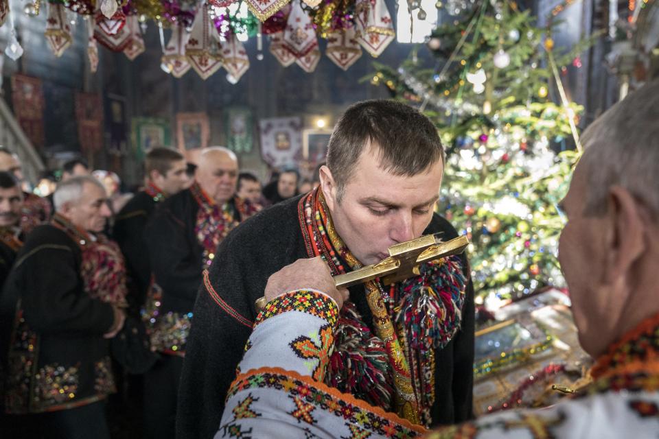 An ethnic Hutsul man, an ethnic group spanning parts of western Ukraine, wearing traditional colorful clothes, kisses a priest's cross during the Orthodox Christmas celebration in the Holy Trinity church in Iltsi village, Ivano-Frankivsk region of Western Ukraine, Thursday, Jan. 7, 2021. Hundreds of maskless parishioners in Verkhovyna lined up at the local church to kiss the icons and the priest's cross during the Christmas service. Ukraine is struggling to contain the coronavirus pandemic that has inundated its overburdened medical system, as Dr. Viktoria Mahnych goes door to door providing much needed help to patients.(AP Photo/Evgeniy Maloletka)