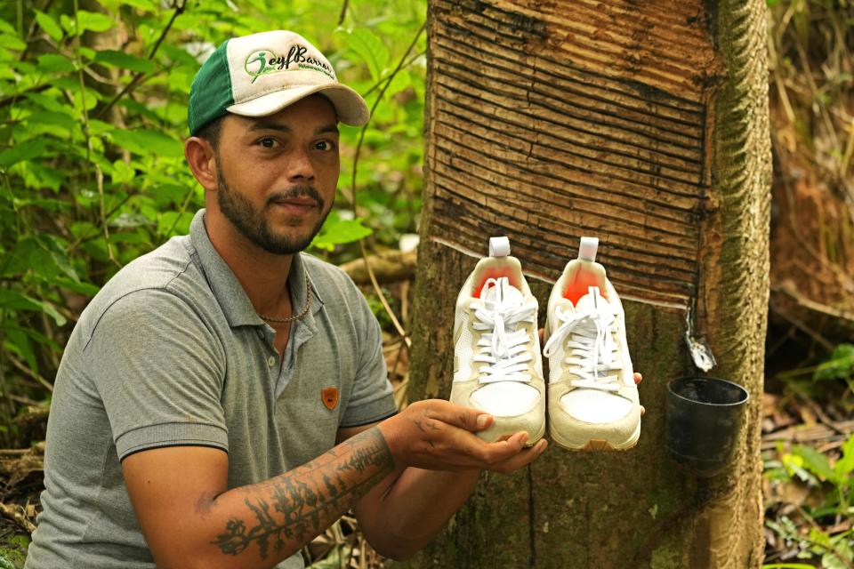 Rubber tapper Rogerio Mendes shows off his Veja sneakers, received as a prize for his work as a young rubber extractor in the Chico Mendes Extractive Reserve, Acre state, Brazil, Wednesday, Dec. 7, 2022. Veja, an expensive global sneaker brand, is producing sneaker soles made of native Brazilian Amazon rubber in collaboration with local rubber tappers cooperatives. "They are making young people come back. They rekindled the hope of working with rubber even if it is a work in progress," Mendes said. (AP Photo/Eraldo Peres)