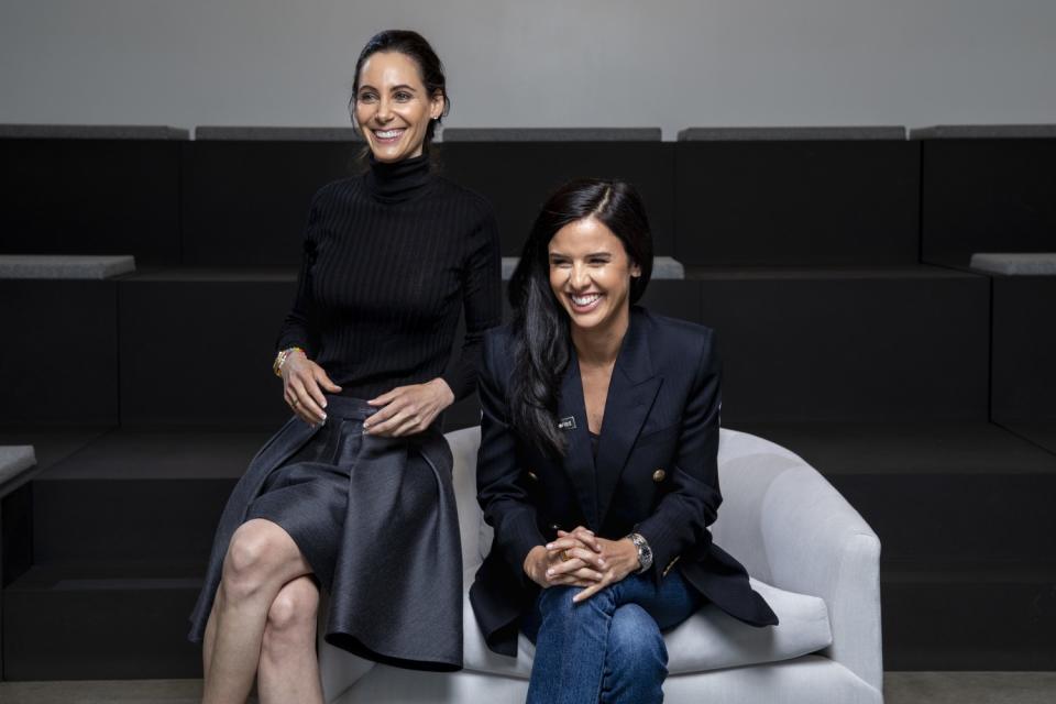 Two women sit next to each other on a chair.