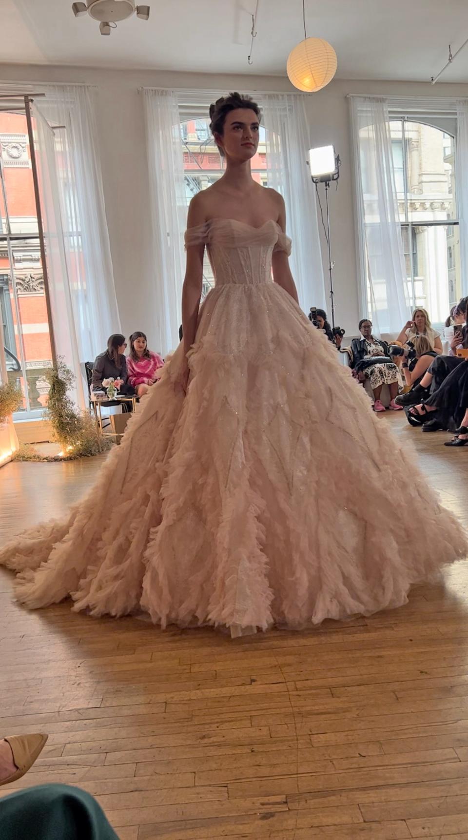 A woman poses in an off-the-shoulder pink wedding dress.