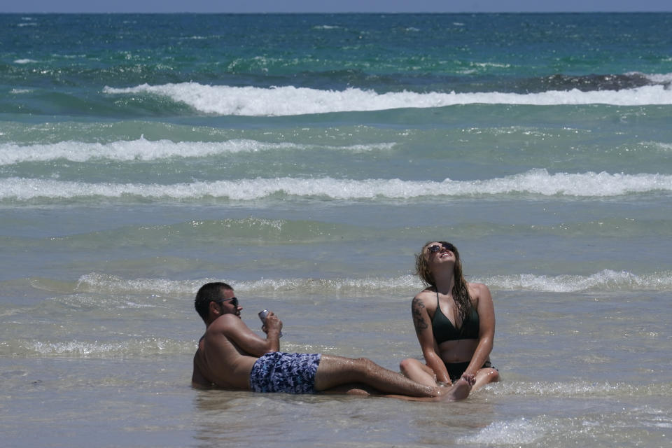 A couple enjoys the beach while sitting on a sandbar, Wednesday, May 26, 2021, in Miami Beach, Fla. The nation's tourist destinations are facing a severe worker shortage just as they try to rebound from a year lost to the coronavirus pandemic. (AP Photo/Marta Lavandier)