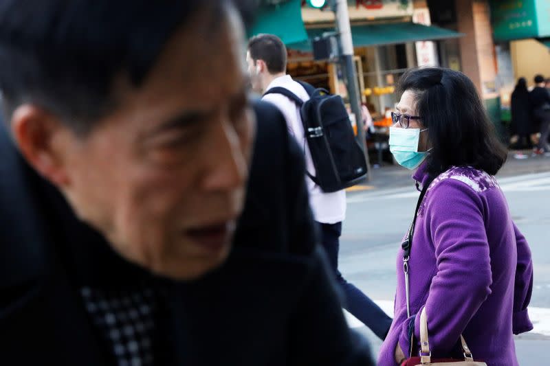 A woman wears a face mask standing on a corner in the Chinatown section of San Francisco, California