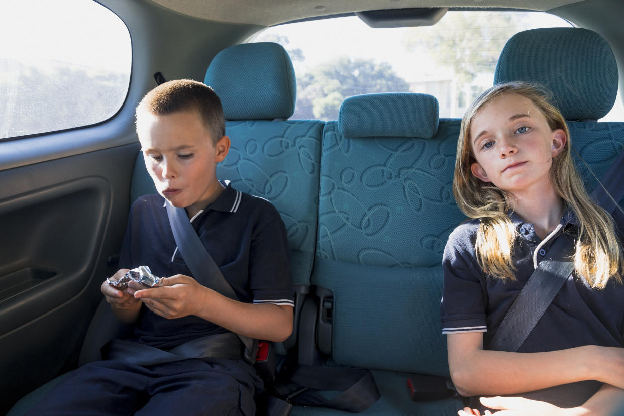 A shot of young, Caucasian boy and girl sitting in the back of the car commuting to school.