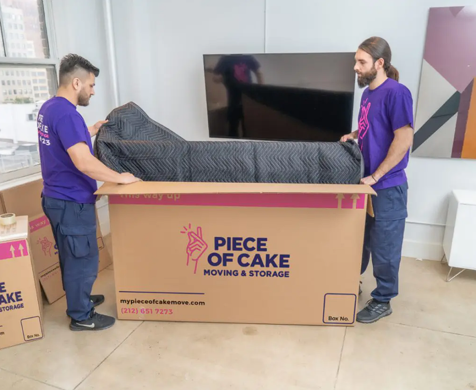 Two staffers for Piece of Cake Moving & Storage safely pack away furniture in a box.