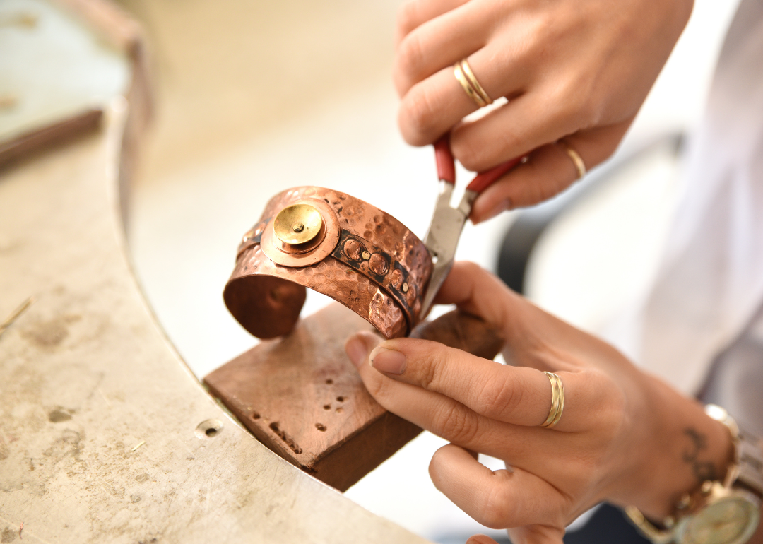 A close up of woman's hands holding pliers while working on a bracelet.