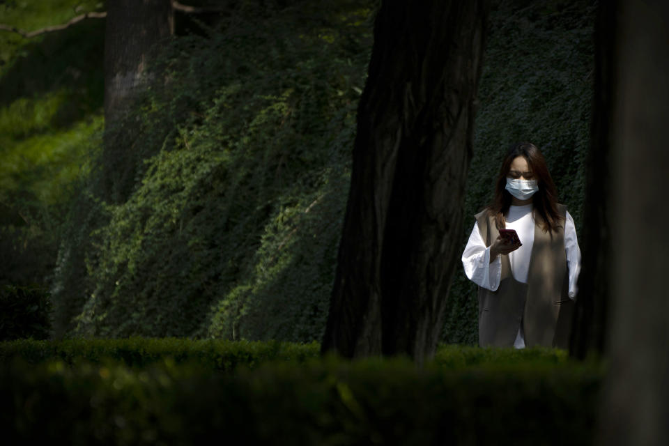 A woman wearing a face mask walks along a path at a public park in Beijing, Tuesday, Aug. 30, 2022. (AP Photo/Mark Schiefelbein)