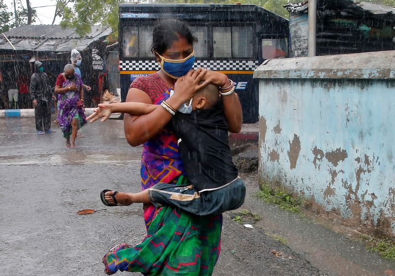 A woman carries her son to a safer place before Cyclone Amphan makes its landfall, in Kolkata
