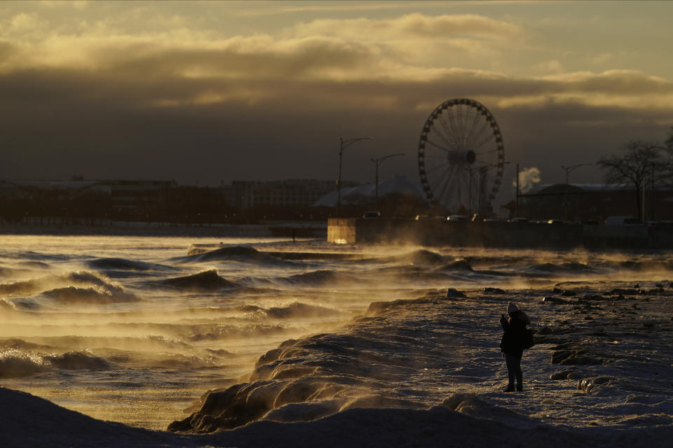 A person takes a picture of the waves crashing on to the shore as ice forms on Oak Street Beach Friday, Feb. 3, 2023, in downtown Chicago. (AP Photo/Kiichiro Sato)