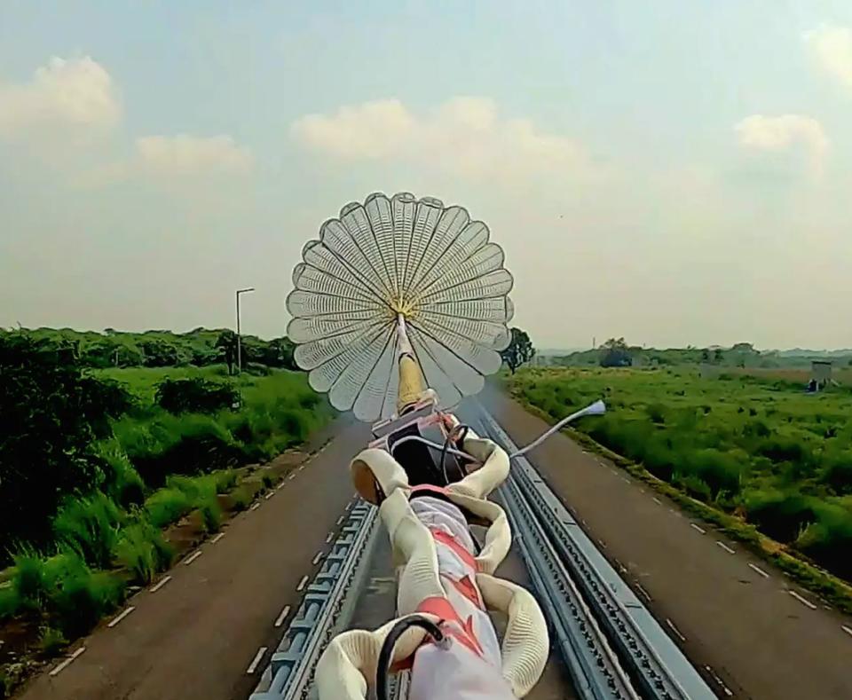 a parachute is pulled along train tracks in a green landscape.