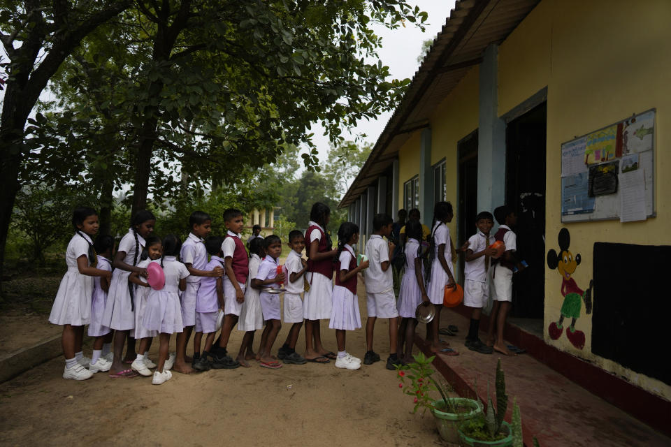 Primary students queue up to receive a free meal given as apart of a feeding program at the Dalukana Primary School in Dimbulagala, about 200 kilometres north east of Colombo, Sri Lanka, Monday, Dec. 12, 2022. (AP Photo/Eranga Jayawardena)