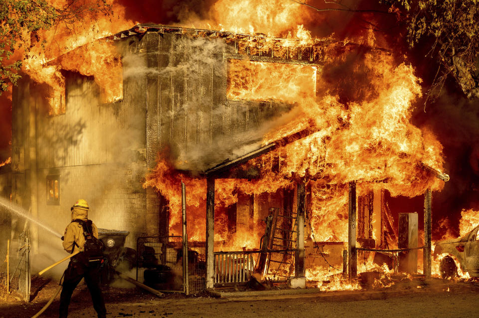 A firefighter sprays water while trying to stop the Sugar Fire, part of the Beckwourth Complex Fire, from spreading to neighboring homes in Doyle, Calif., Saturday, July 10, 2021. Pushed by heavy winds amid a heat wave, the fire came out of the hills and destroyed multiple residences in central Doyle. (AP Photo/Noah Berger)