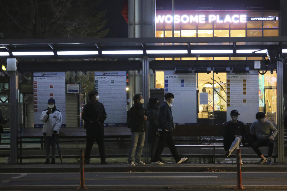 People wearing face masks to help protect against the spread of the coronavirus wait for buses at a bus station in Goyang, South Korea, Sunday, Nov. 22, 2020. South Korea says it will impose stricter social distancing rules in the greater Seoul area to fight a coronavirus resurgence, as the country registered more than 300 new cases for the fifth straight day. (AP Photo/Ahn Young-joon)