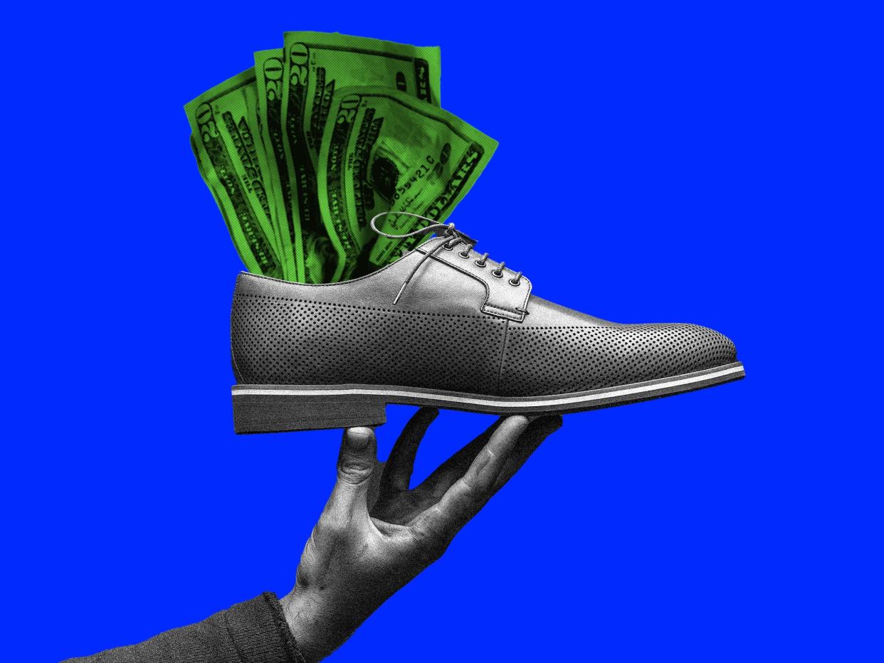 A hand holding up a men's shoe with money in it