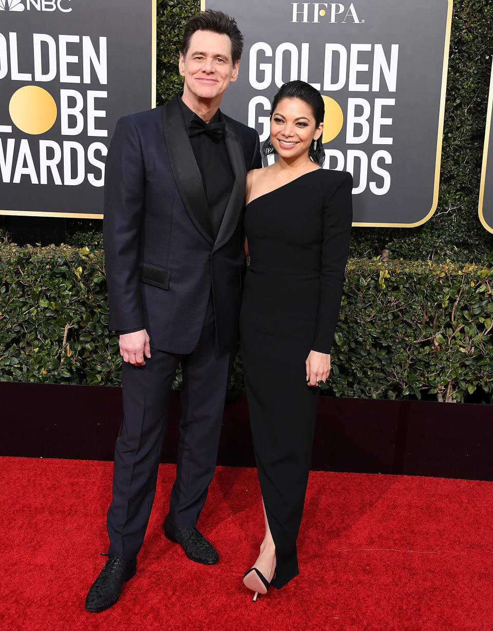 Two celebrities standing together at the Golden Globe Awards; one in a black suit and the other in a black evening gown