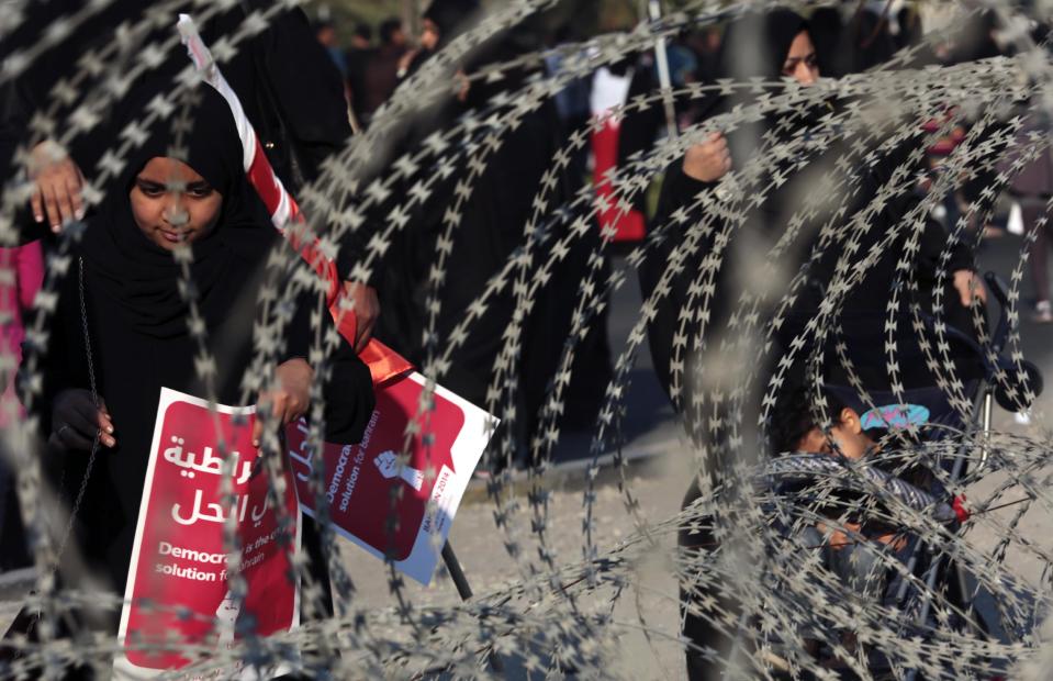 A Bahraini girl places a sign that reads in Arabic, "democracy is the solution," into razor wire coiled outside a police station near Muqaba, Bahrain, during a pro-democracy march west of the capital of Manama, on Saturday, Feb. 15, 2014. Tens of thousands of protesters marched down a divided four-lane highway, calling for the long-serving prime minister, Sheik Khalifa bin Salman Al Khalifa, to step down and for democracy in the Gulf island kingdom. (AP Photo/Hasan Jamali)