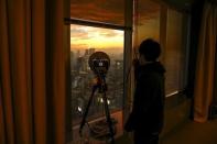 A TV technician talks with his newsroom about the signal strength a device is transmitting from the news conference room on 39th floor of the Toshiba head office as the sun sets over Tokyo, Japan, December 21, 2015. REUTERS/Thomas Peter