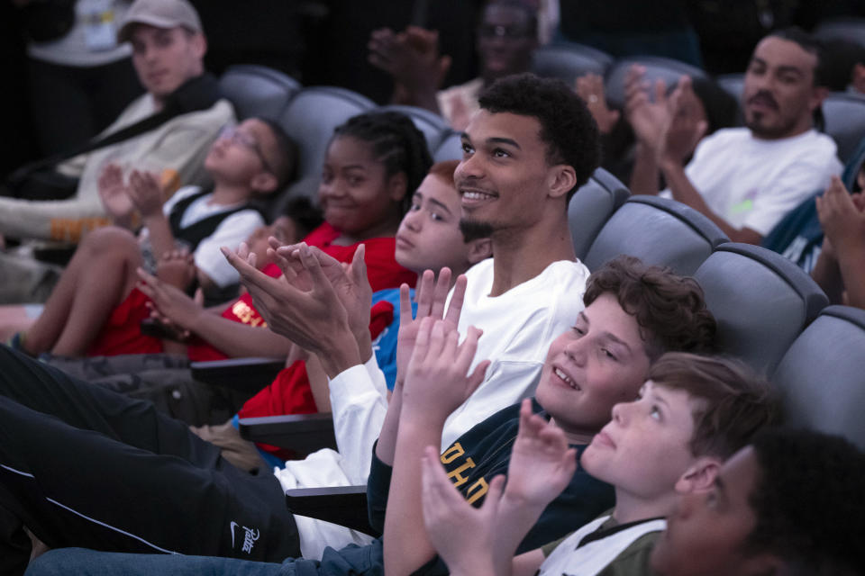 San Antonio Spurs' Victor Wembanyama, center, watches videos with local children before receiving his 2023-24 NBA Rookie of the Year trophy, Saturday, May 11, 2024, in San Antonio. (AP Photo/Darren Abate)