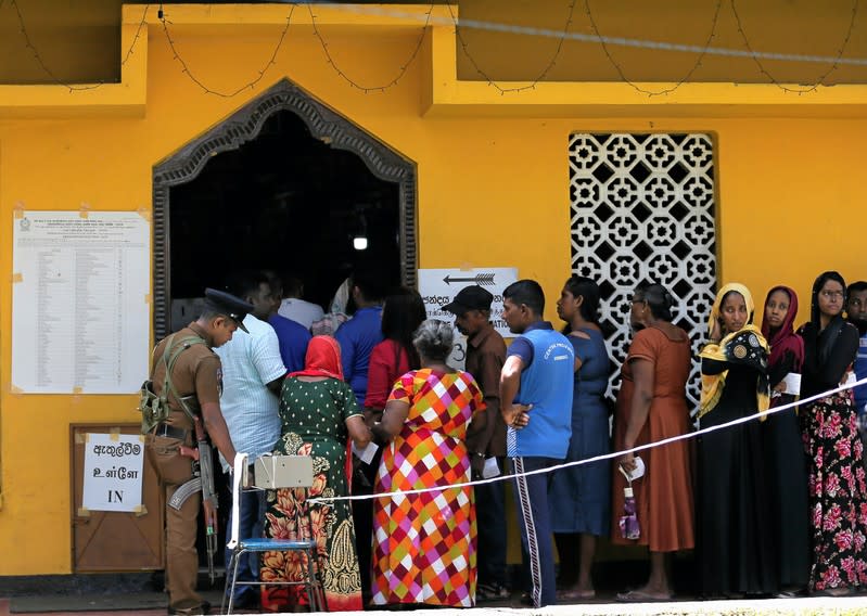 A police offier is seen as people stand in a line to cast their vote during the presidential election in Colombo