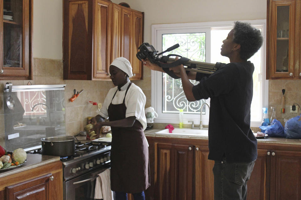 In this Nov. 24, 2018, photo, filmmaker Tuleka Prah, right, films chef Touty Sarr , as she prepares a pot of thiebou dieune, a traditional Senegalese dish of spiced rice, inside a kitchen in Ngaparou, Senegal. In the quiet hours before lunch, two women worked side by side in an airy kitchen. One, a chef, cleaned fresh red snapper filets with a sharp knife. The other, a filmmaker, pointed her camera into a large pot of simmering vegetables. (AP Photo/Amelia Nierenberg)